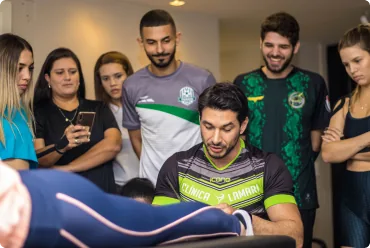 Participantes acompanhando demonstração de bandagem na perna, um deles filmando com o celular