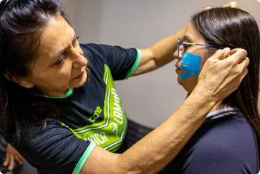 Dra. Neuseli Lamari aplicando bandagem elástica azul no rosto de uma participante