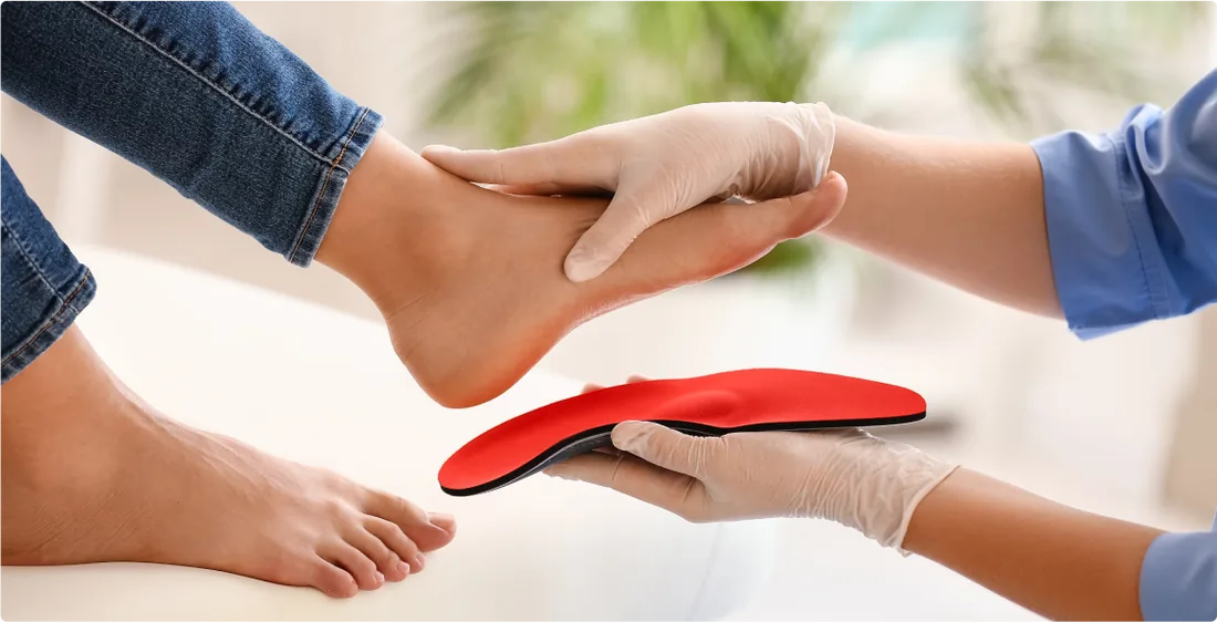 Mãos de profissional ajustando uma palmilha postural vermelha sobre o pé de um paciente